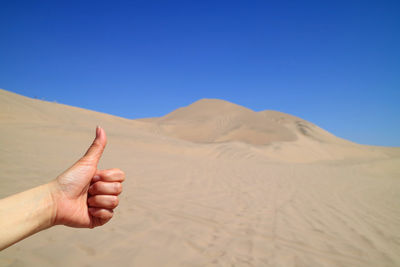 Cropped hand showing thumbs up at desert against sky