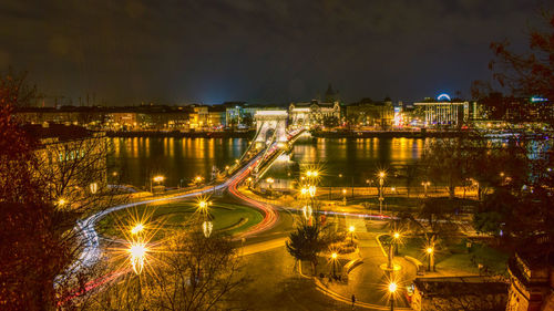 Illuminated city by river against sky at night