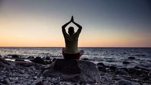 Man standing on rock by sea against sky during sunset