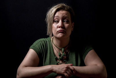 Young woman making face against black background