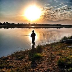 Silhouette man standing by lake against sky during sunset