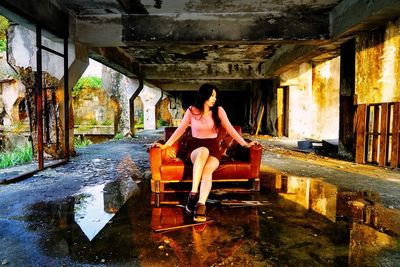 Full length of woman sitting on chair in abandoned building