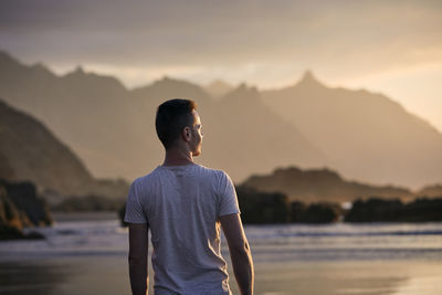 Rear view of pensive man on beach aganinst cliff at golden sunset. beautiful nature in tenerife.