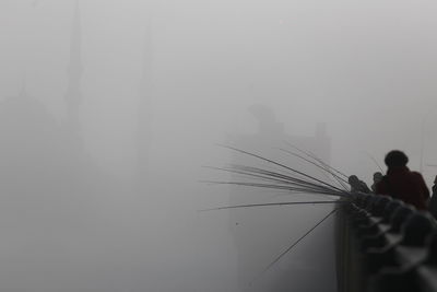 Silhouette people standing on foggy weather against sky