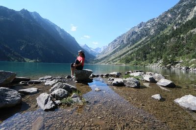 Woman looking at lake while sitting on rock against mountains
