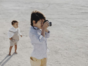 Kid takes photo with vintage camera as other kid stands in background