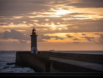 Lighthouse by sea against sky during sunset