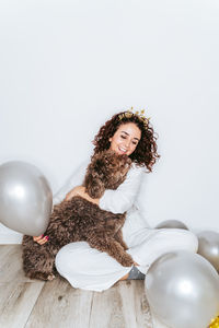 Smiling woman sitting with dog against wall at home