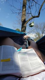 Midsection of woman reading book against tree