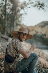 Portrait of man wearing hat sitting on land