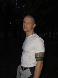 Portrait of young man standing against trees at night