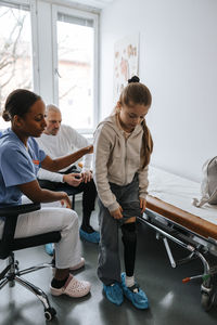 Girl with artificial limb standing next to female doctor in medical examination room at clinic