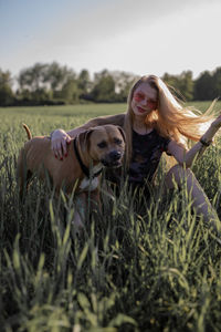 Young woman with dog sitting on grassy field against clear sky