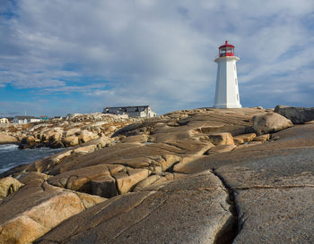 Lighthouse amidst rocks and buildings against sky