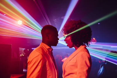 Happy black couple dancing against colorful neon illumination during party in nightclub