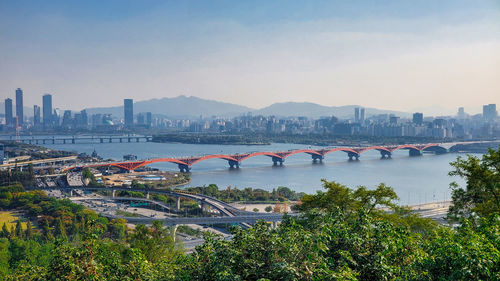 Bridge over river by buildings against sky