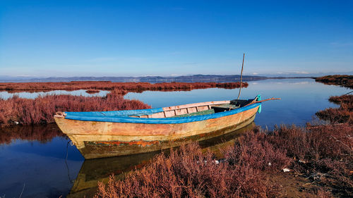 Boats moored on lake against clear blue sky