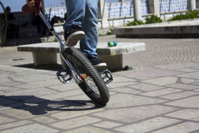 Low section of man riding unicycle on footpath in city