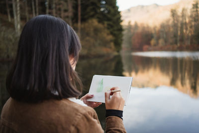 Rear view of woman holding umbrella against lake