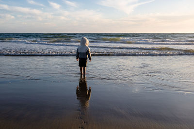 Rear view of woman standing on beach against sky