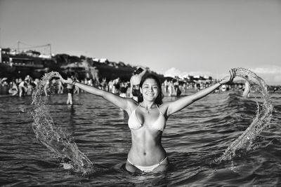 Portrait of young woman wearing bikini while splashing water in sea