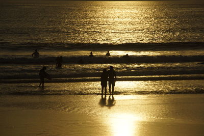 Silhouette people standing on beach against sky during sunset