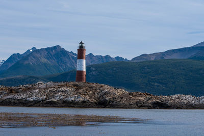 Lighthouse amidst buildings and mountains against sky