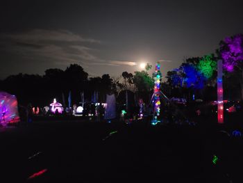 Silhouette people on illuminated road against sky at night