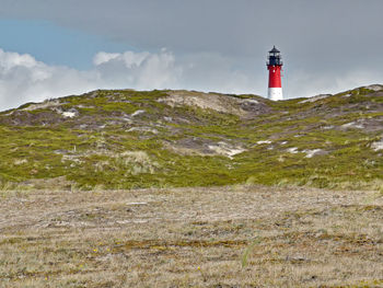 Lighthouse on road amidst buildings against sky