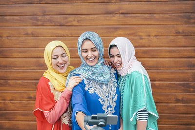 Happy female friends taking selfie by wall