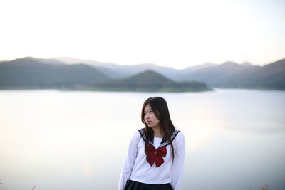 Young woman standing by lake against sky