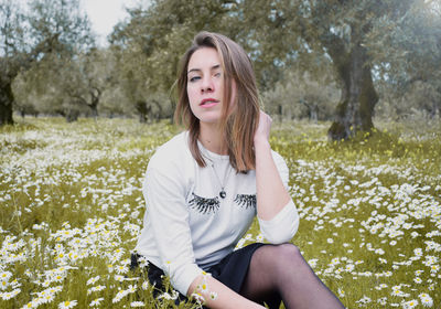 Portrait of woman with hand in hair sitting amidst flowers blooming on field