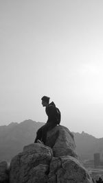 Man sitting on rock against sky