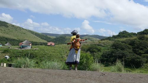 Rear view of mother carrying baby boy while standing against mountains