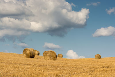 Hay bales in fields against clouds