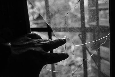 Close-up of hand by broken glass window