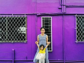 Portrait of woman standing with daughter outside purple building