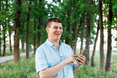 Young man using mobile phone while standing on tree