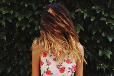 Woman with tousled hair standing against leaves