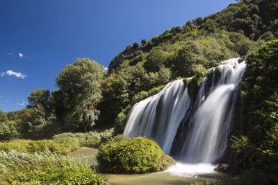 Low angle view of waterfall in forest against clear blue sky