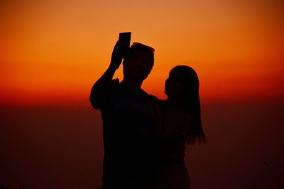 Silhouette of woman photographing orange sunset sky