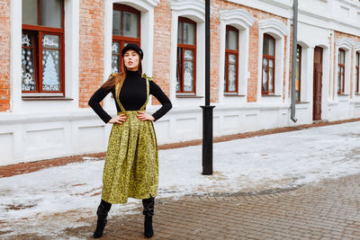 Portrait of young woman standing on road against building during winter