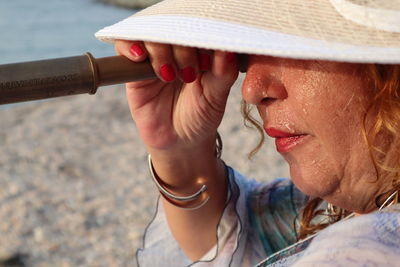 Close-up of woman wearing hat while looking through binoculars