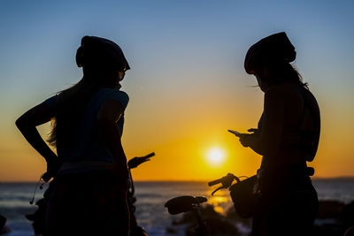 Silhouette people at beach against sky during sunset