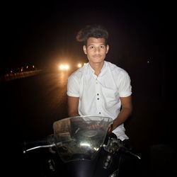 Portrait of young man sitting on motorcycle at road during night