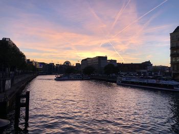 River by buildings in city against sky during sunset