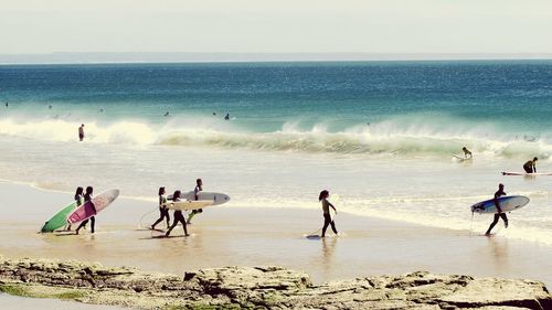 People with surfboards walking at beach on sunny day