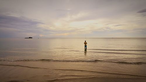 Man standing on beach against sky during sunset