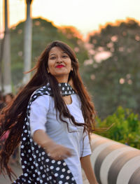 Portrait of smiling young woman with tousled hair against trees