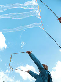 Low angle view of man jumping against blue sky